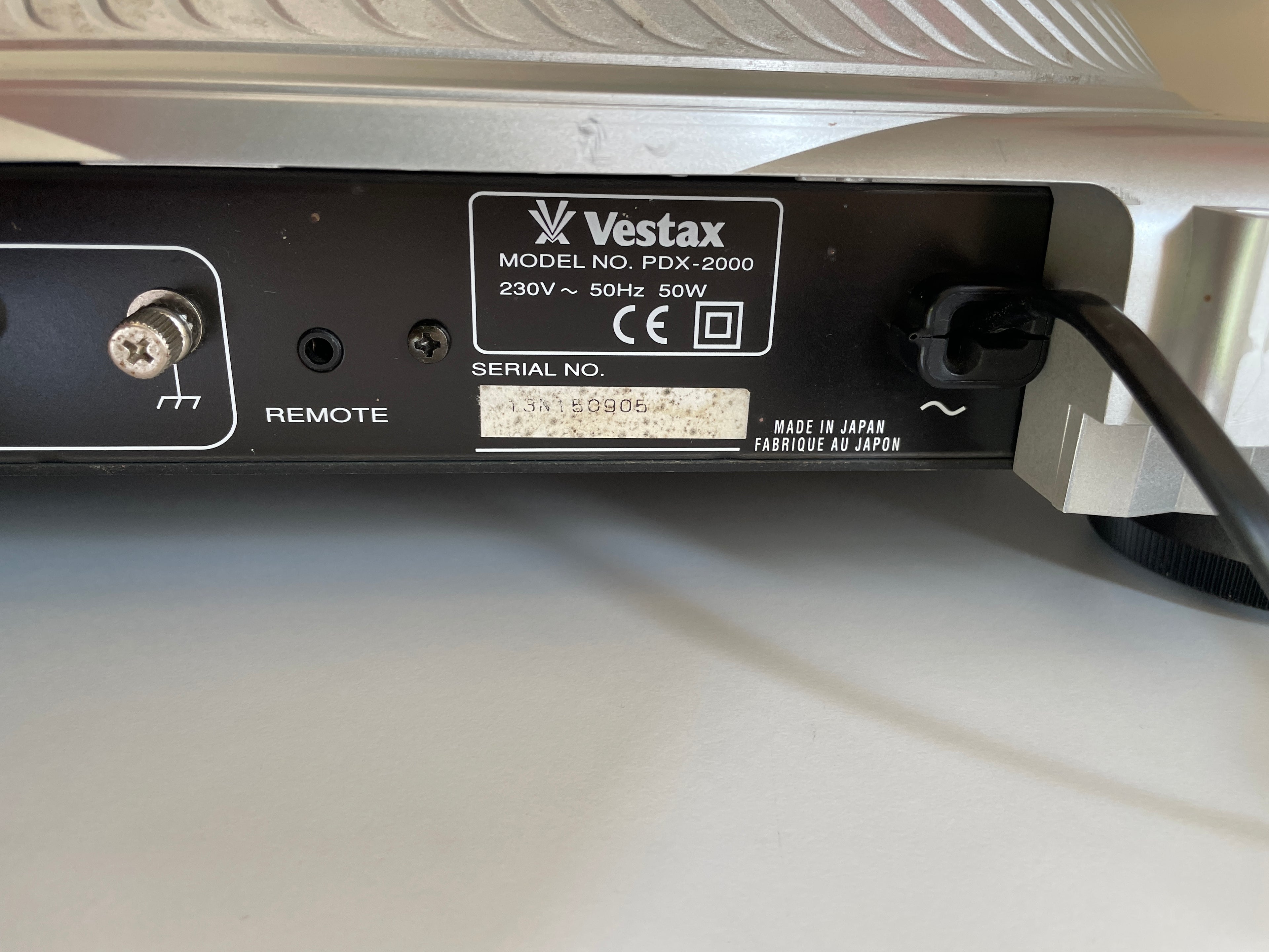 Close-up of the rear panel of a Vestax PDX-2000 electronic device, showing the brand label, remote control port, power plug, and serial number on a white surface.