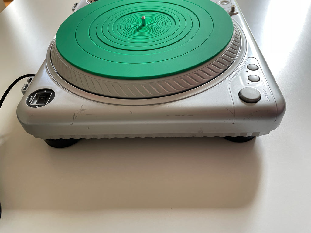 A silver DJ turntable with a bright green plinth and matching green tonearm, photographed from a top-down angle on a white surface.