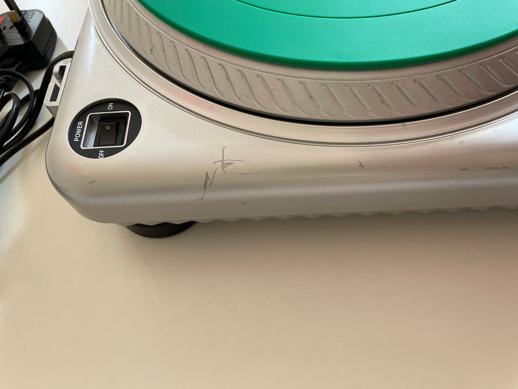 Close-up of a silver and black electronic device with a green circular dial, showing a power switch labeled POWER and ON/OFF, photographed against a beige wall.