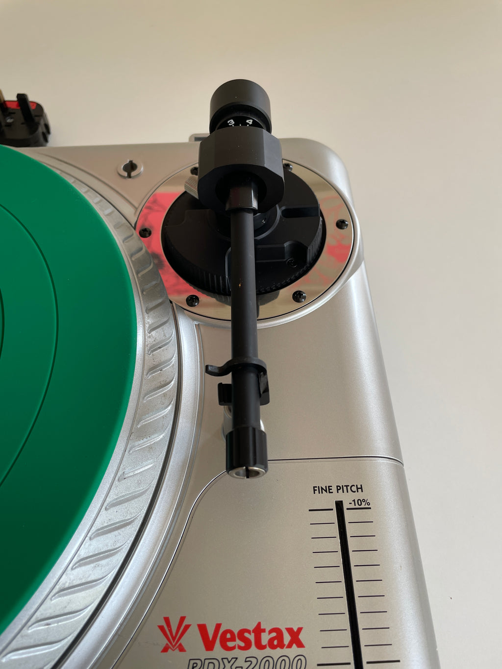 Close-up of a Vestax PDX-2000 turntable showing the silver outer shell, a green platter, and a black tonearm.