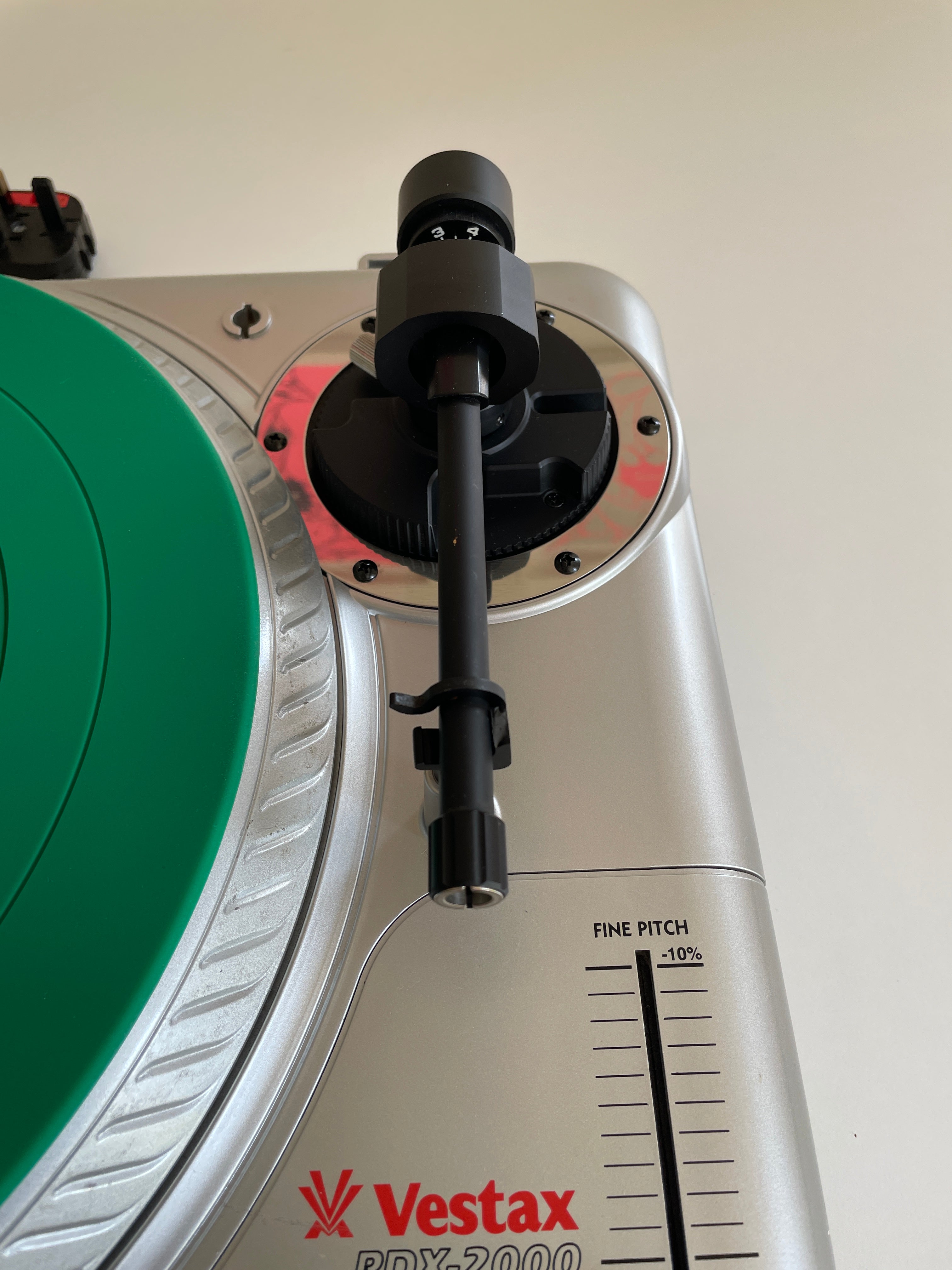 Close-up of a Vestax PDX-2000 turntable showing the silver outer shell, a green platter, and a black tonearm.
