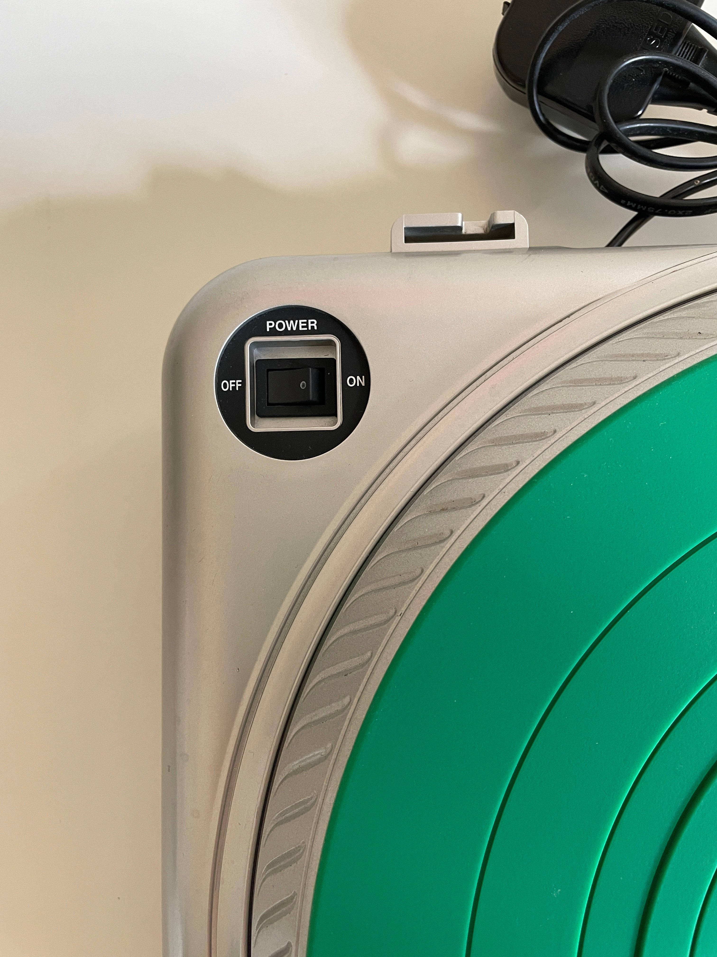 Close-up of a silver appliance showing a black power switch labeled OFF and ON, with a large green circular panel and part of a black power cord visible.