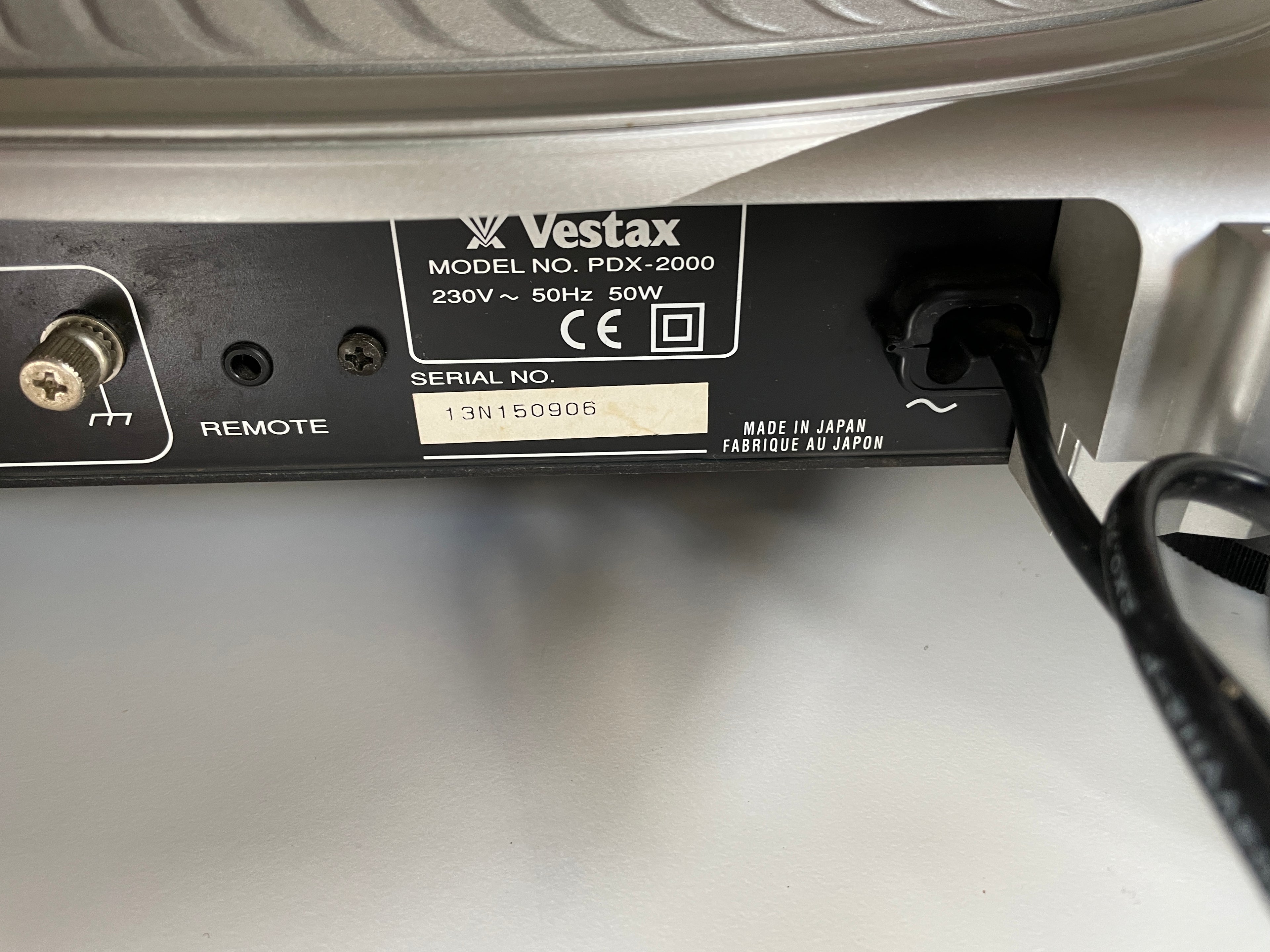Close-up of the back panel of a Vestax PDX-2000 turntable, showing the power adapter plugged in, remote port, and serial number label.