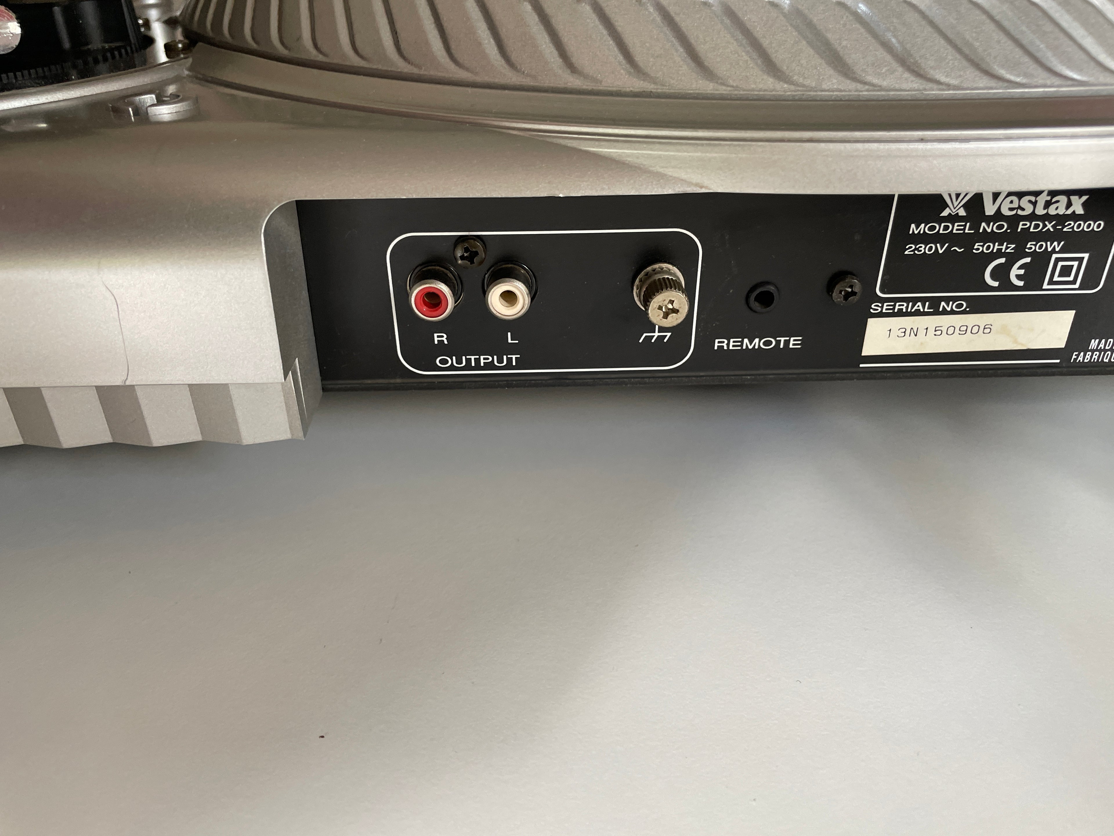 Close-up of the rear output panel of a Vestax PDX-2000 turntable, showing red and white RCA jacks, a 3.5mm headphone jack, a remote button, and a serial number label.