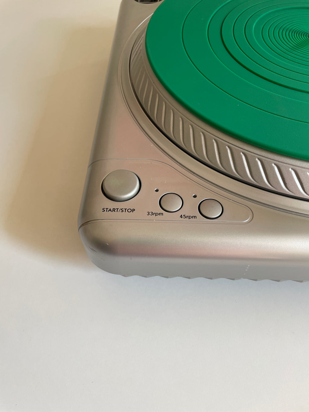 Close-up of a silver electronic device with a green circular dial and three control buttons labeled START/STOP, 33rpm, and 45rpm, on a white surface.