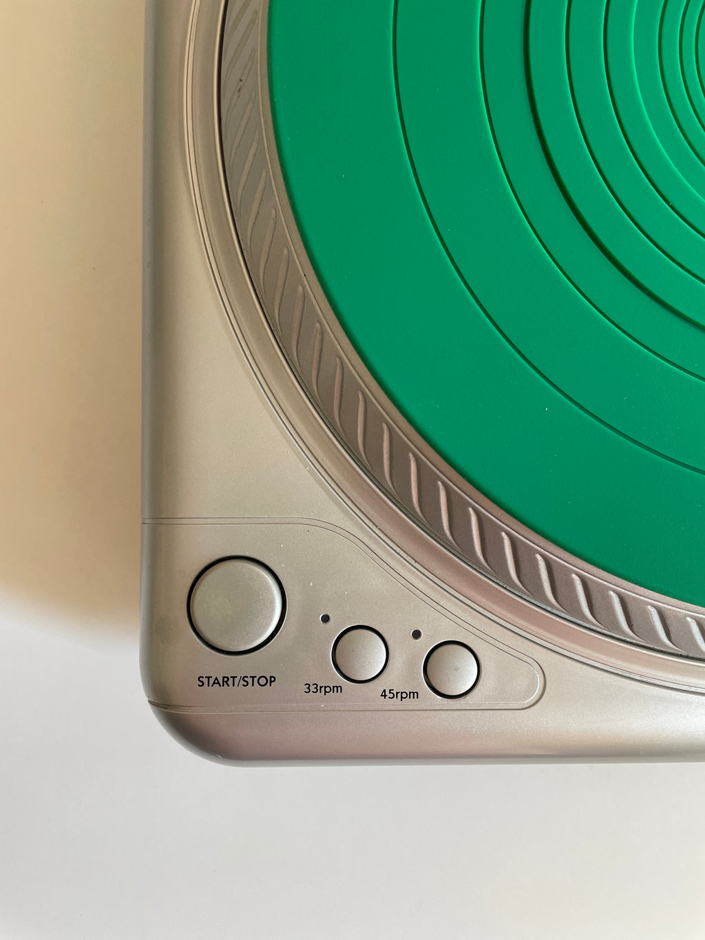 Close-up of a turntable showing the control panel with a green circular dial and silver buttons.