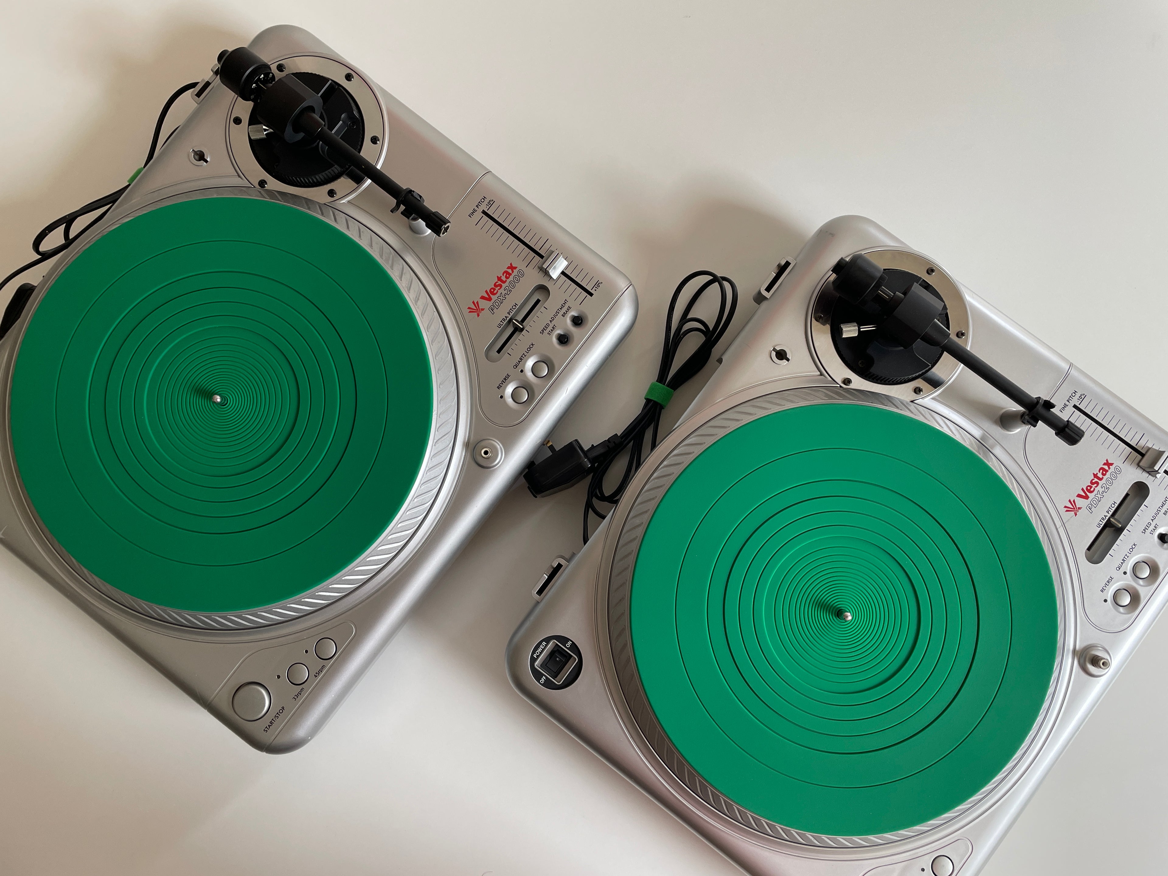 Two silver Vestax PDX 2000 turntables with bright green rubber mats, shown from an overhead angle on a white background.