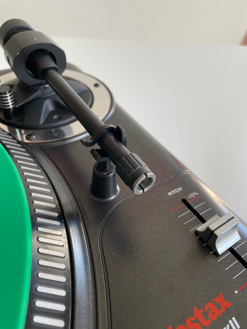 Close-up of a black turntable with a tonearm, featuring a green vinyl record edge and part of the red and white Rega Estax logo.