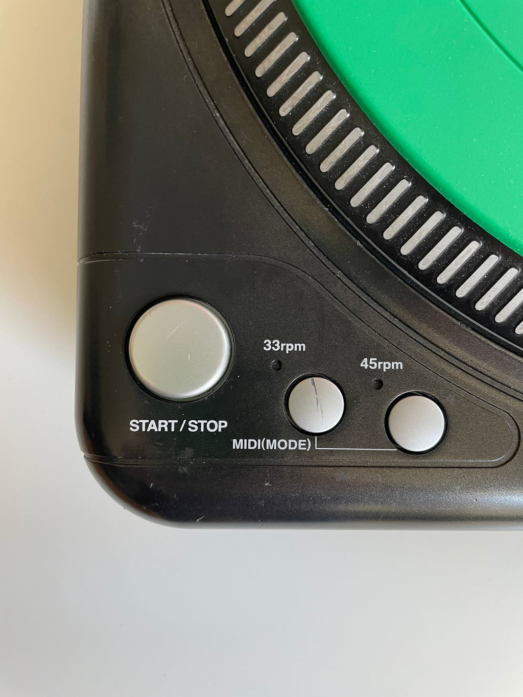 Close-up of a black electronic device showing control buttons labeled START/STOP, 33rpm, MIDI/MODE, and 45rpm, with a green circular section at the top.