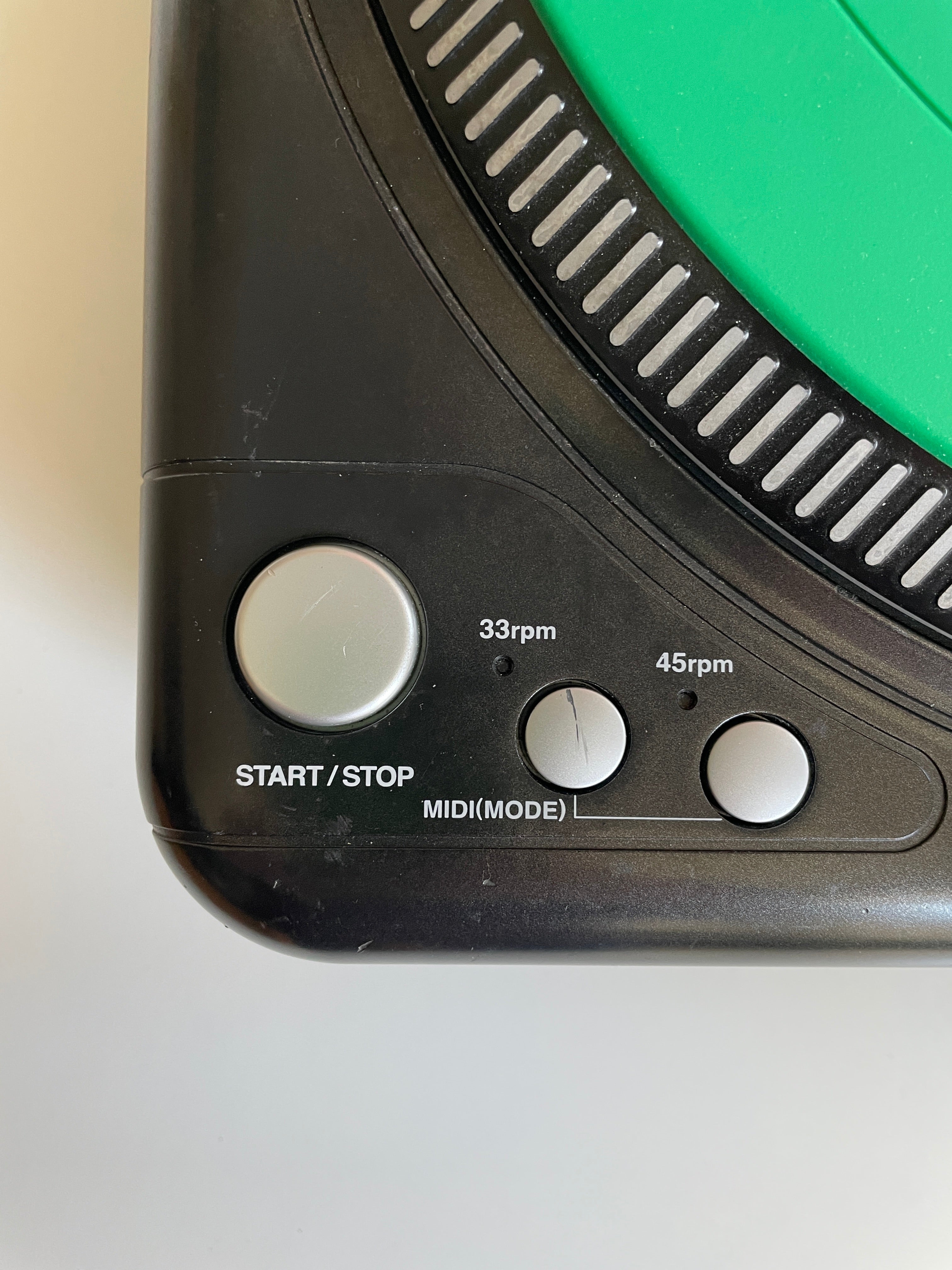 Close-up of a black electronic device showing control buttons labeled START/STOP, 33rpm, MIDI/MODE, and 45rpm, with a green circular section at the top.