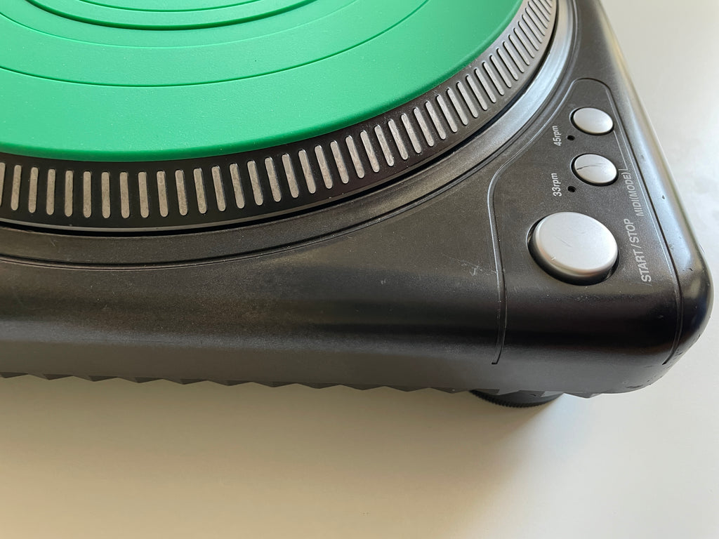 Close-up of a portable electric burner showing its black plastic body, silver control buttons, and a bright green circular heating element on a light surface.