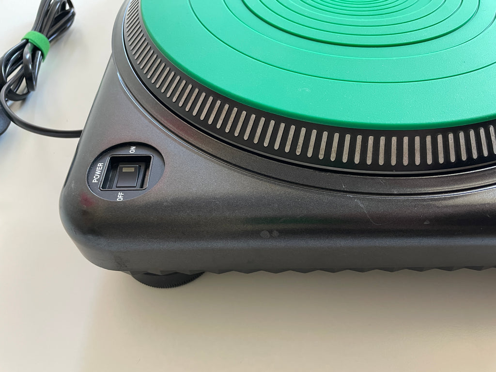 Close-up of a black electric hot plate with a bright green circular heating surface and a power switch labeled Power/Br, on a light beige surface.
