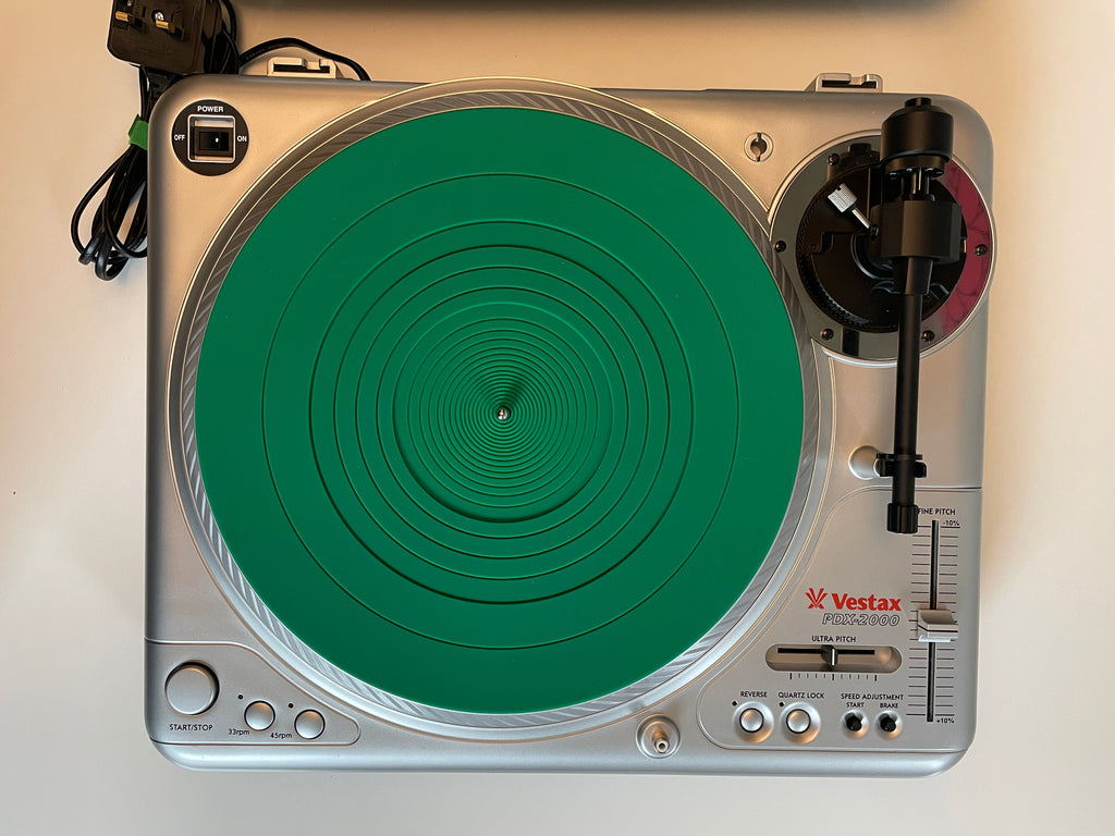 A silver Vostak DJ turntable with a bright green circular protective cover or mat on the platter, photographed from above on a plain light background.