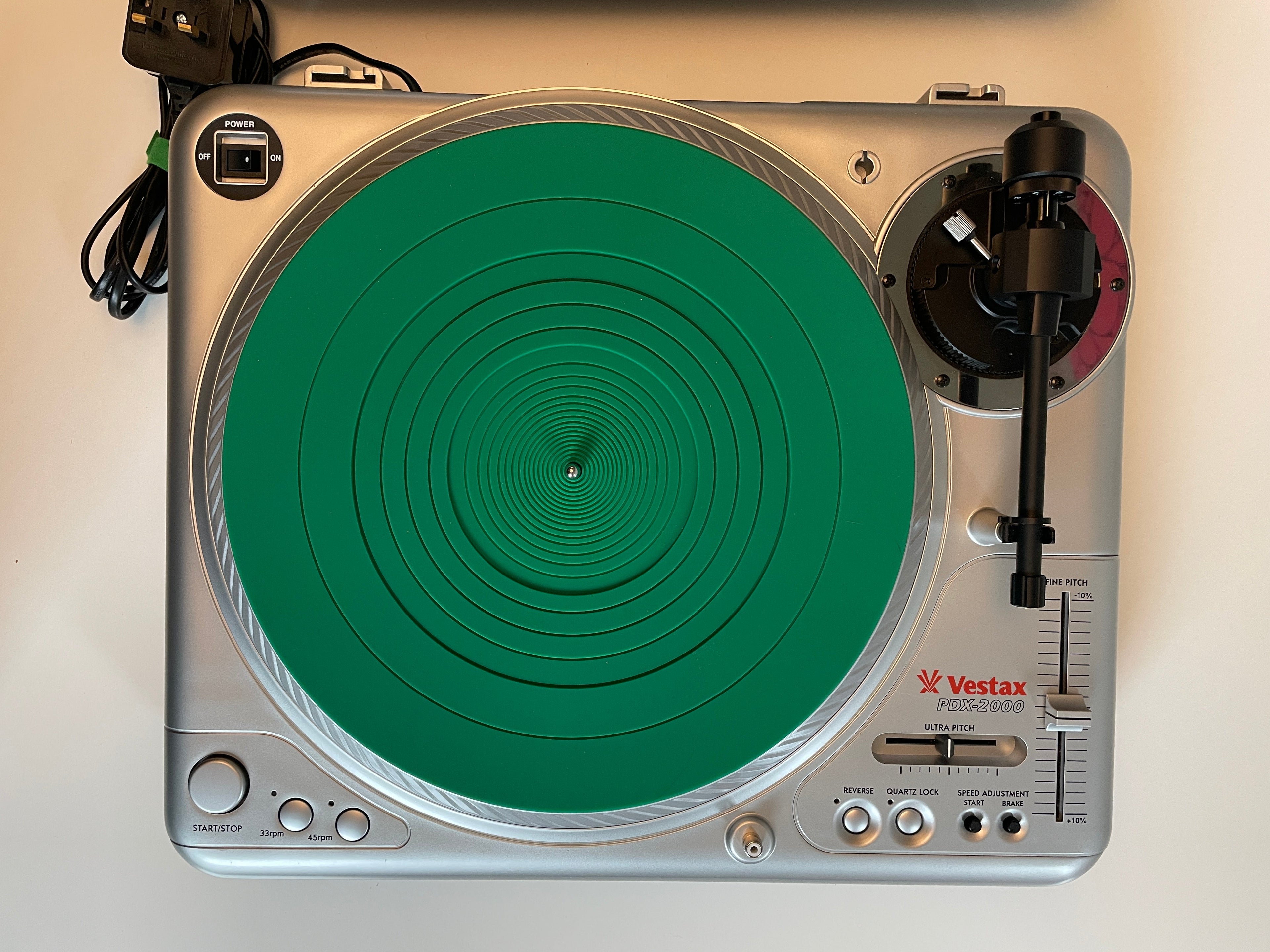 A silver Vostak DJ turntable with a bright green circular protective cover or mat on the platter, photographed from above on a plain light background.