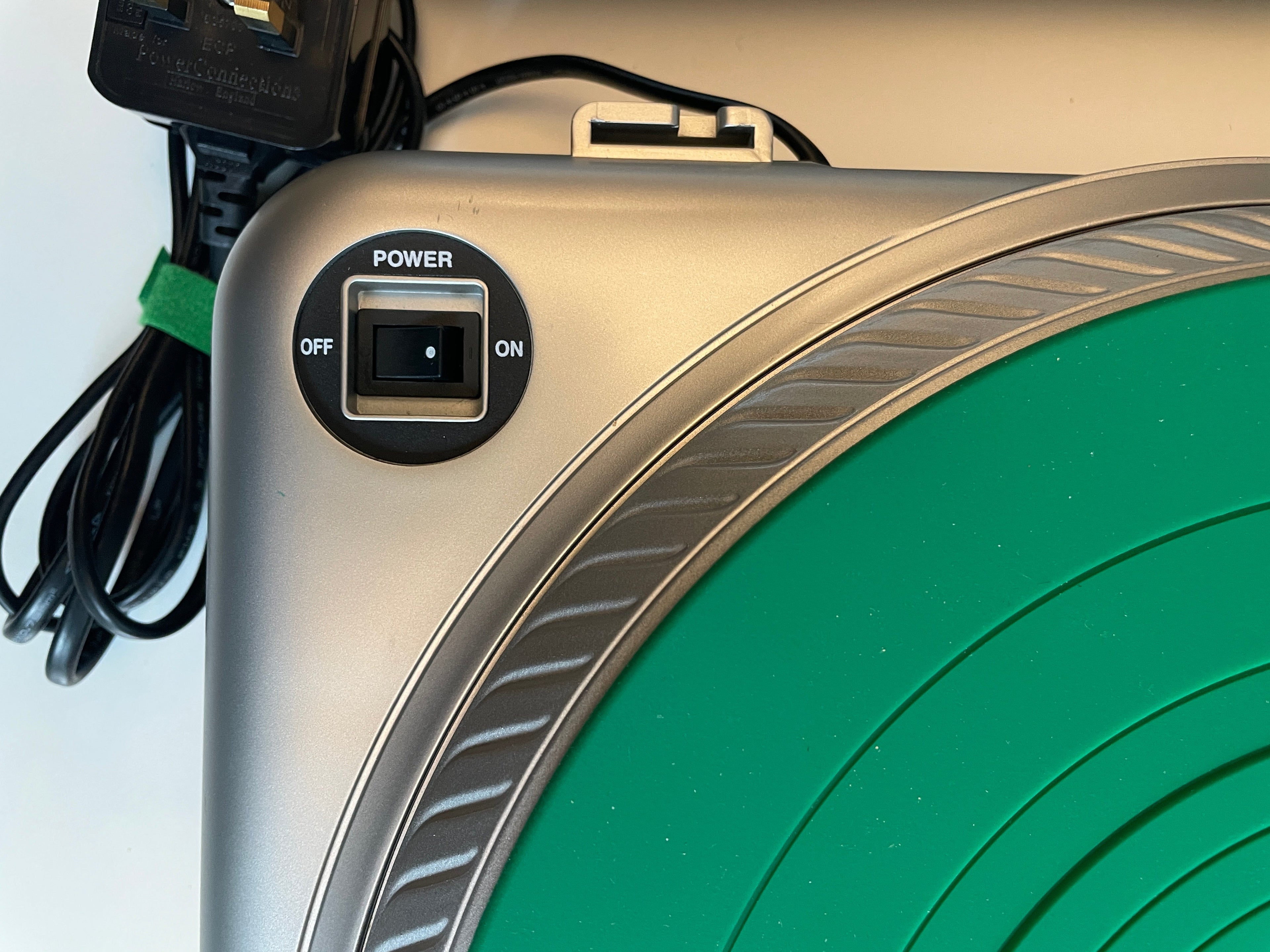 Close-up of a silver and green circular device, showing a power switch labeled POWER ON/OFF and part of the power cord.