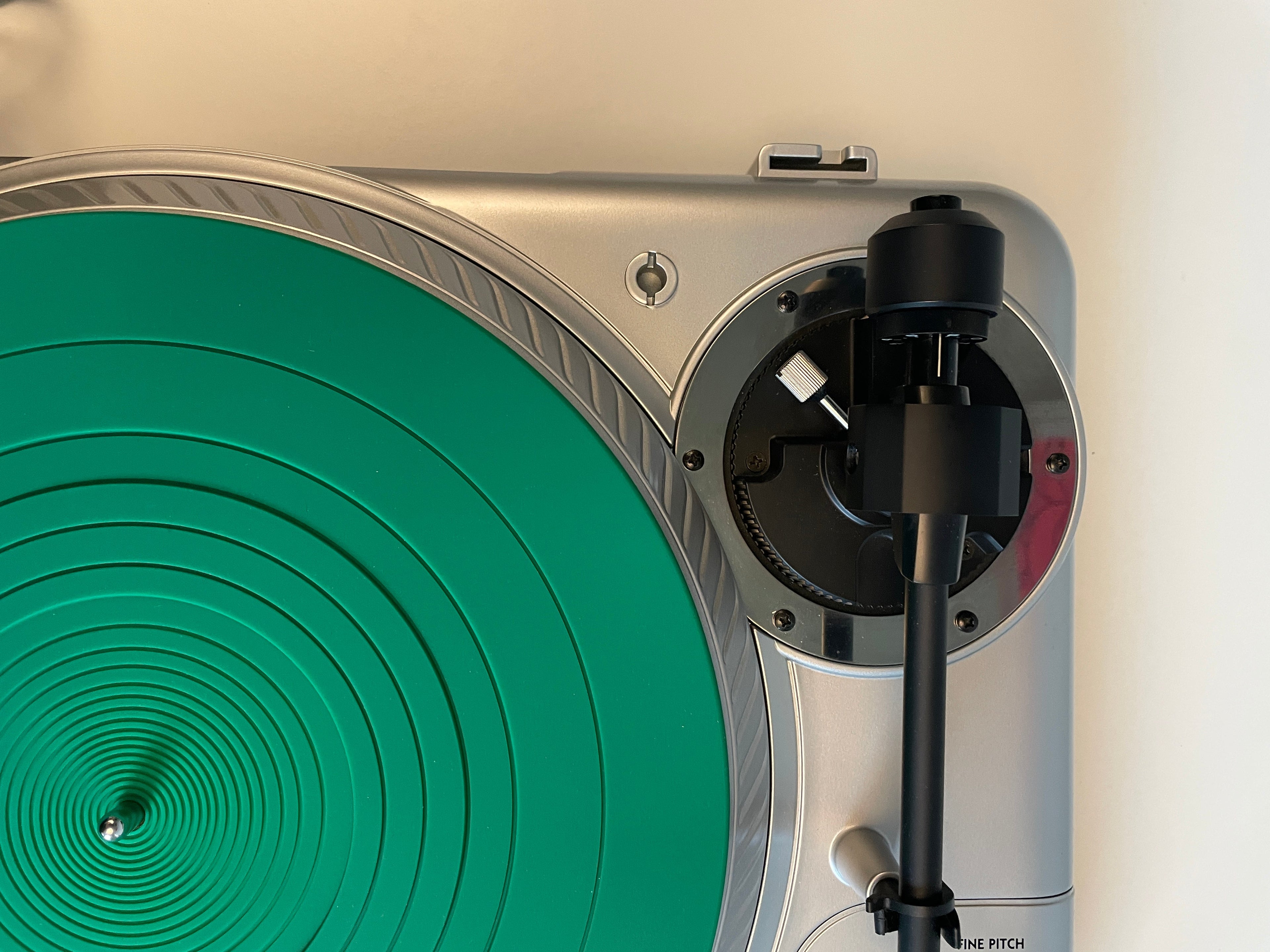 Close-up of a silver record player with a bright green vinyl record on the platter and a black tonearm resting above it.