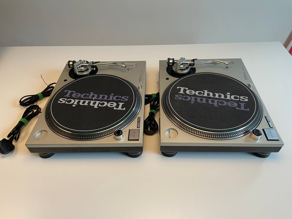 Two Technics turntable platters with black slipcovers and silver metal bodies, placed side by side on a white tabletop against a light gray wall.