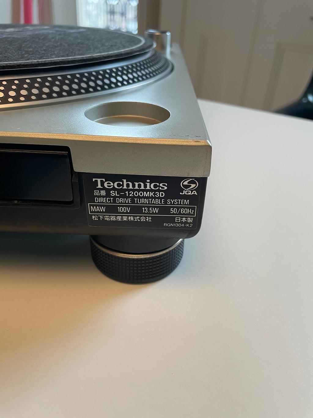 Close-up of a Technics SL-1200MK3D direct drive turntable system, showing the side label and part of the silver and black plinth on a white tabletop.