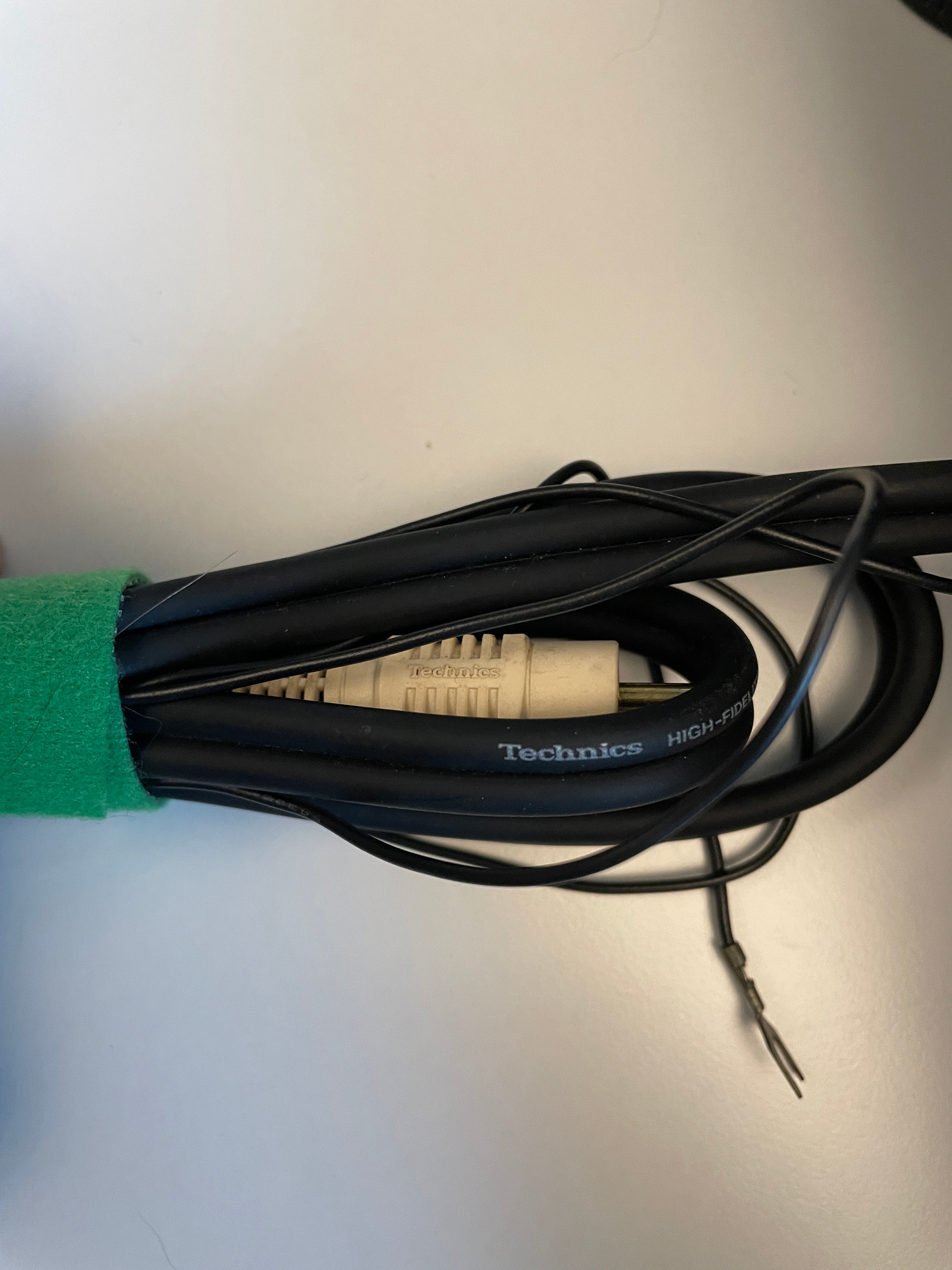 A bundle of black audio cables wrapped together with a green tape measure, featuring a beige RCA connector and a visible Technics brand logo on one cable.