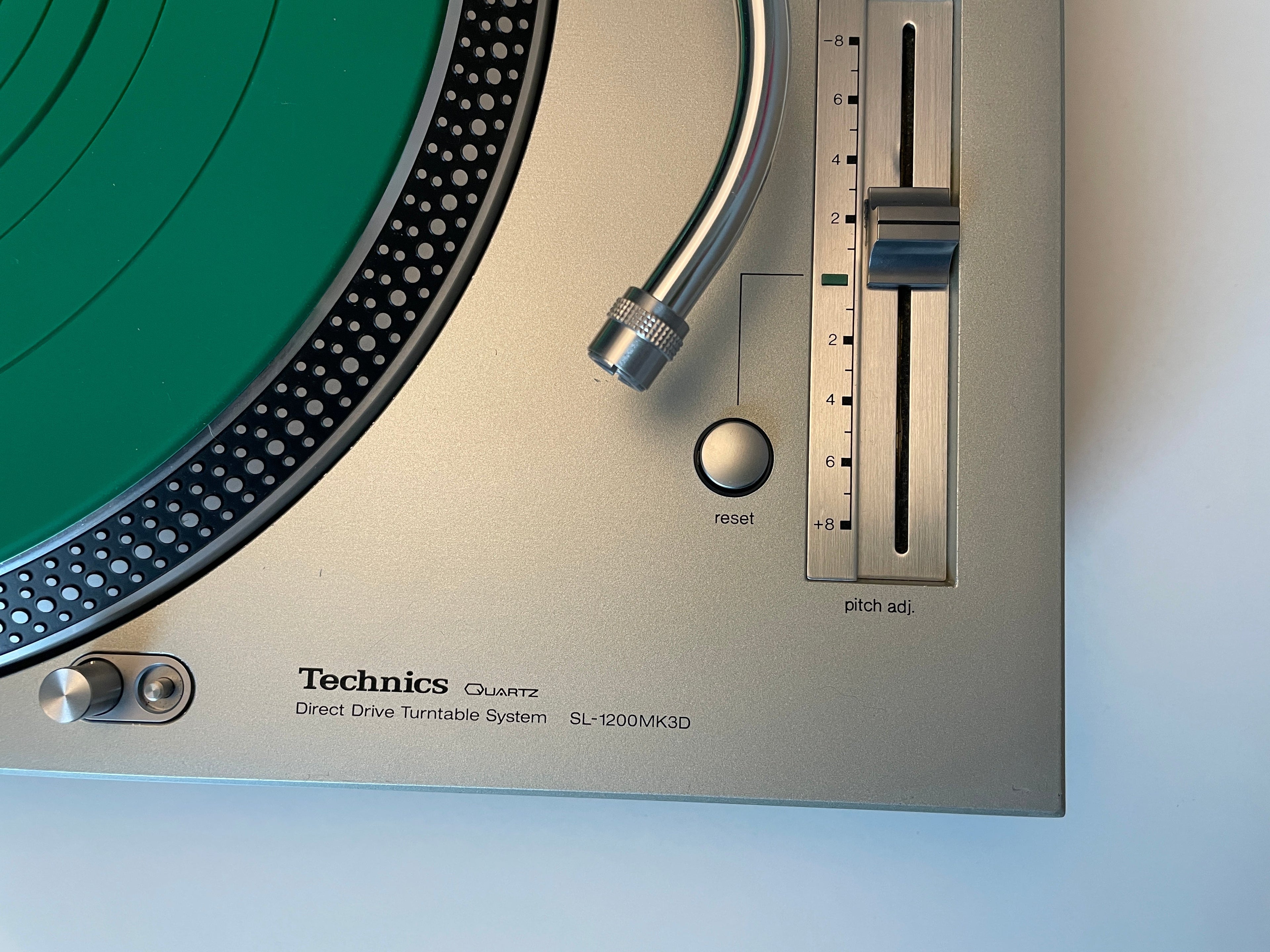 Close-up of a Technics SL-1200MK3D direct drive turntable showing the beige control panel, tonearm, and a green vinyl record.