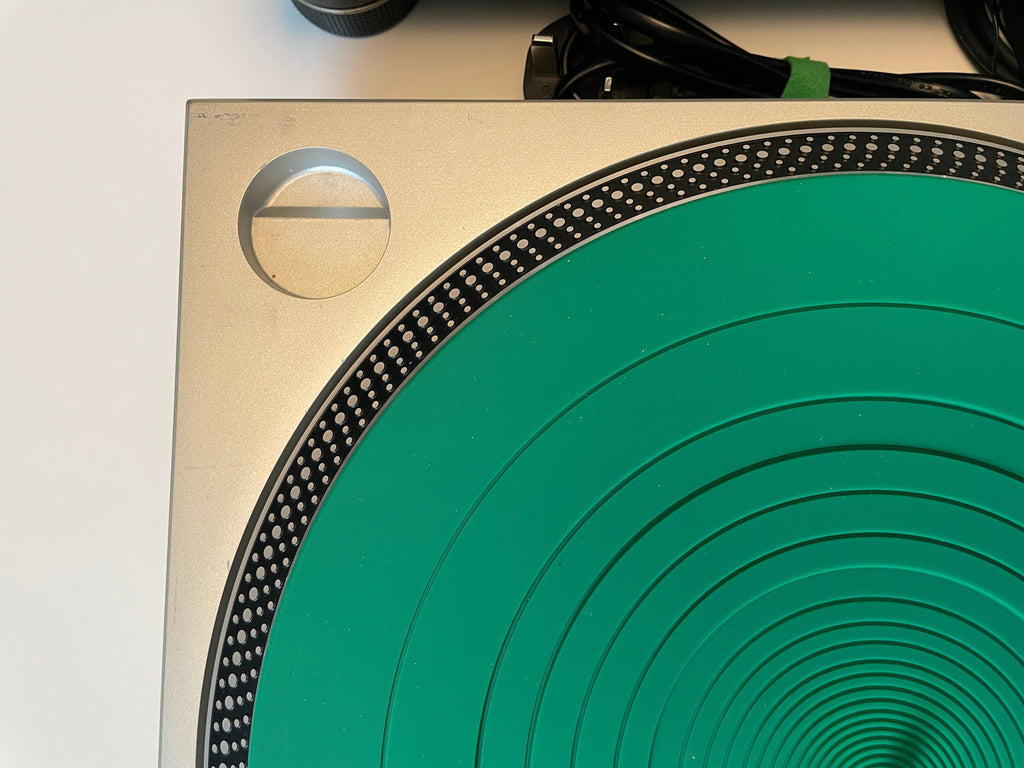 Close-up of a turntable platter with a bright green center and a brushed silver metal outer ring, photographed against a white background.