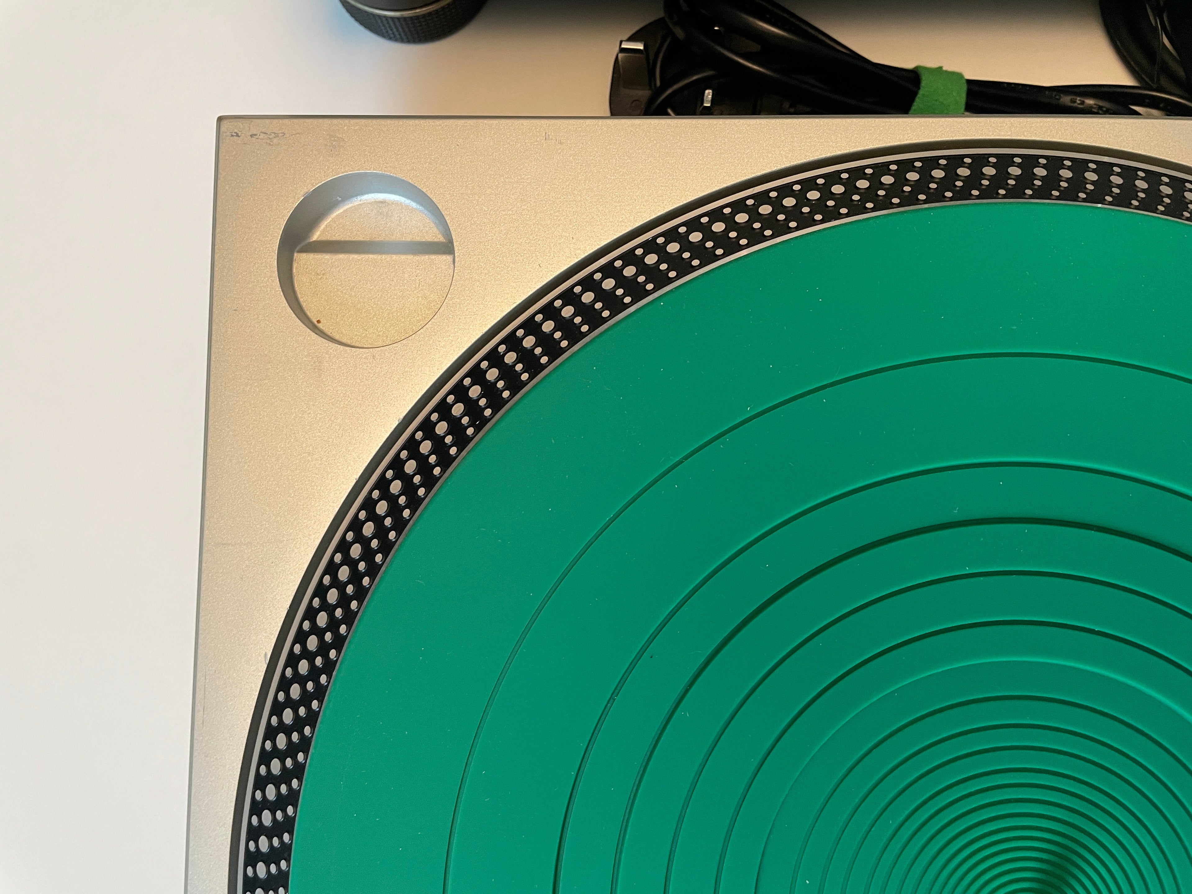 Close-up of a turntable platter with a bright green center and a brushed silver metal outer ring, photographed against a white background.