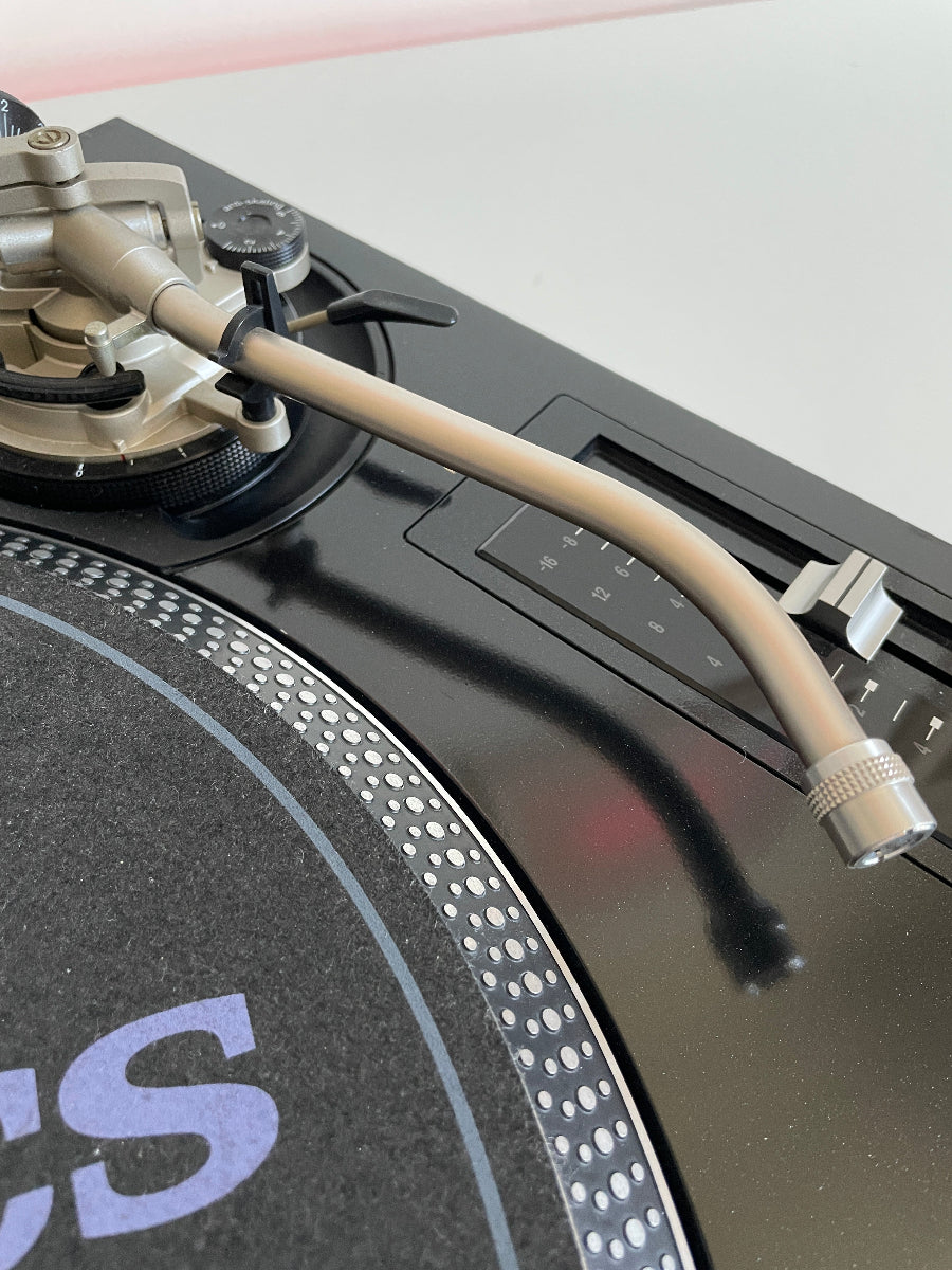 Close-up of a turntable with a cable and control knobs on a light gray background