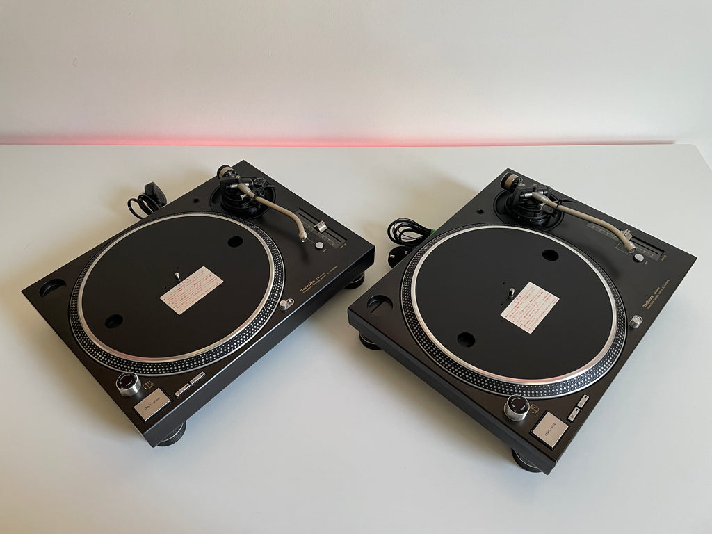 Two black turntables on a white surface with a red light in the background.