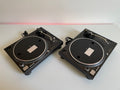 Two black turntables on a white surface with a red light in the background.