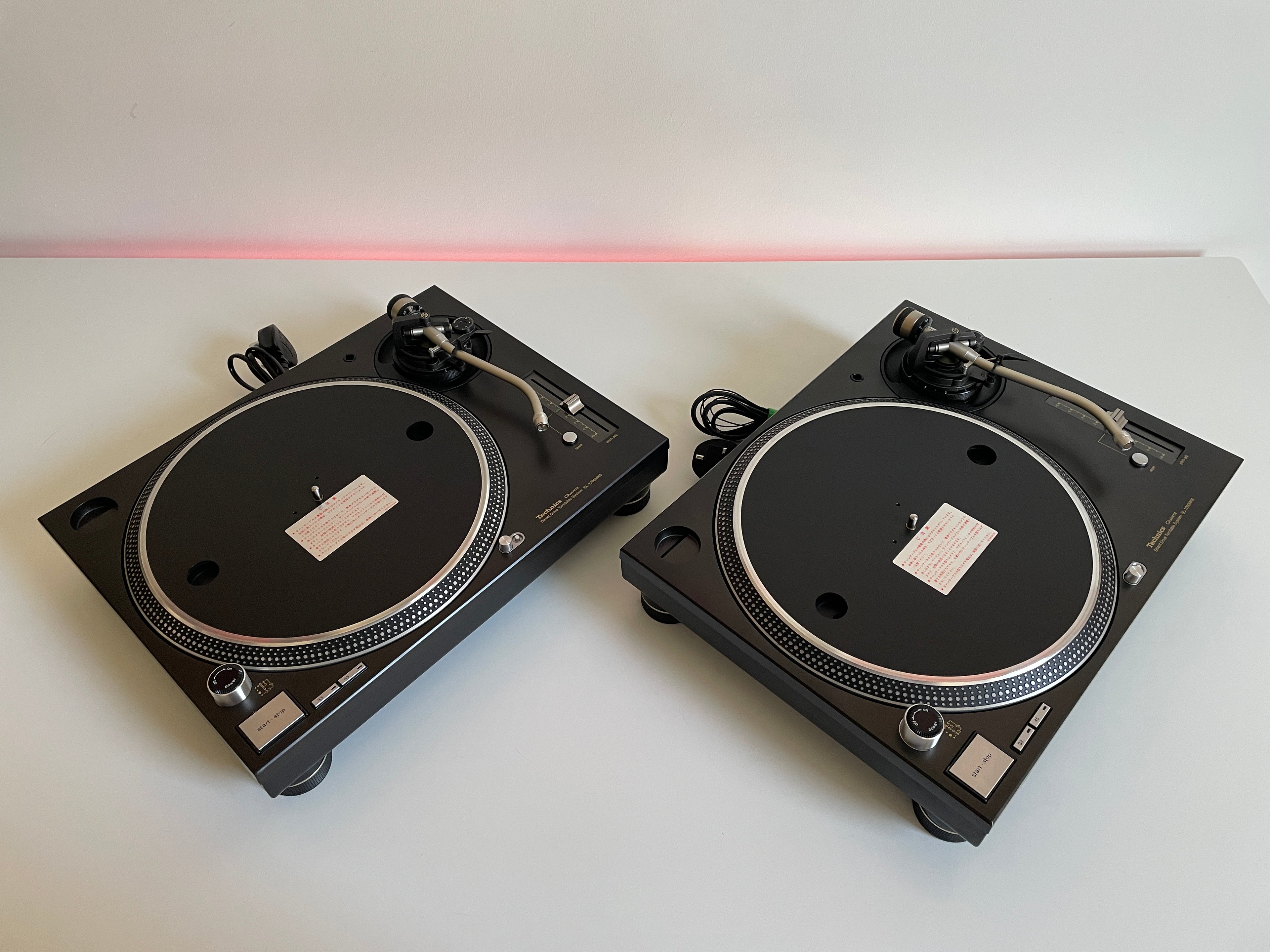 Two black turntables on a white surface with a red light in the background.