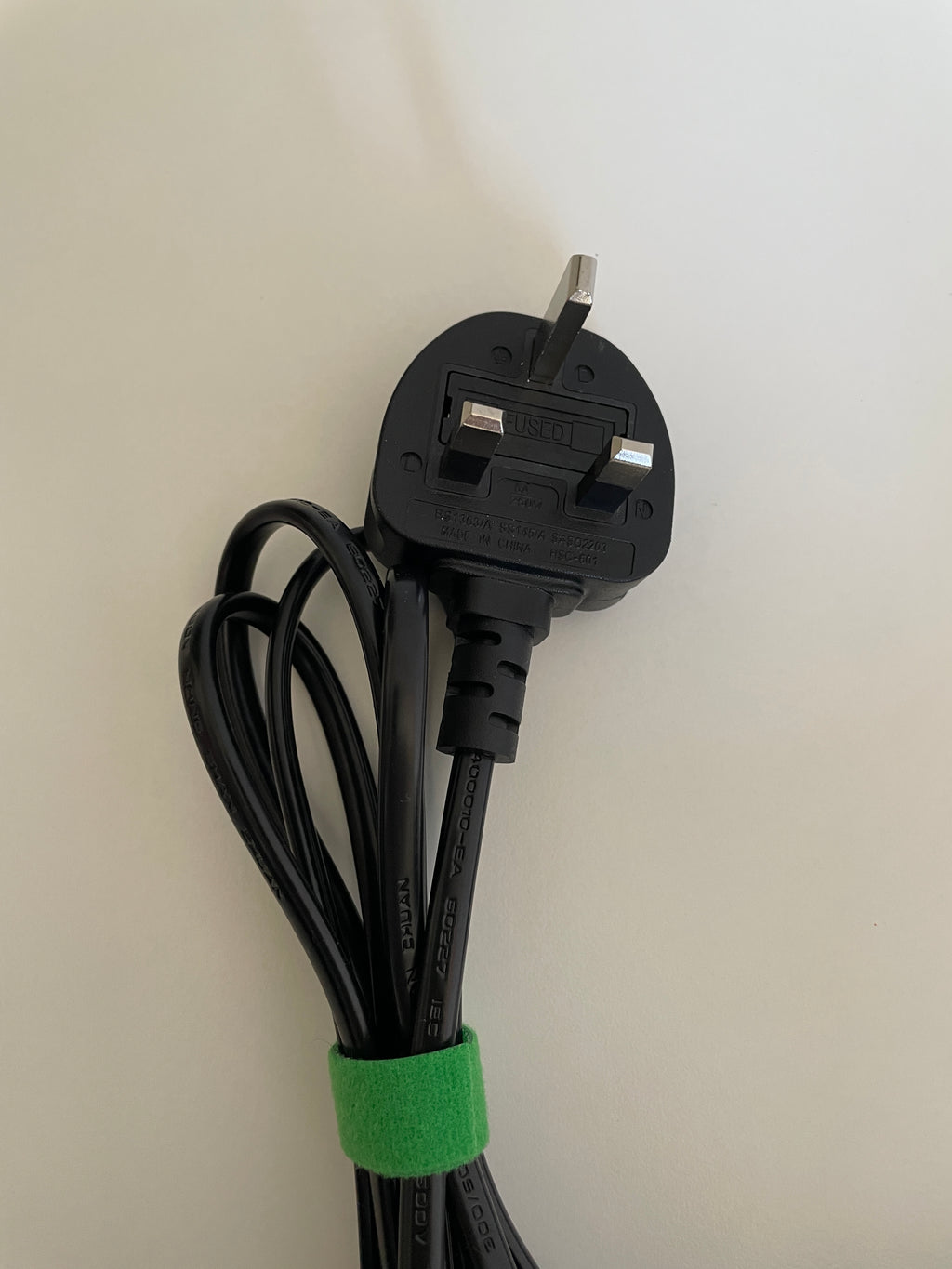 Black electrical plug with a green tie on a beige background