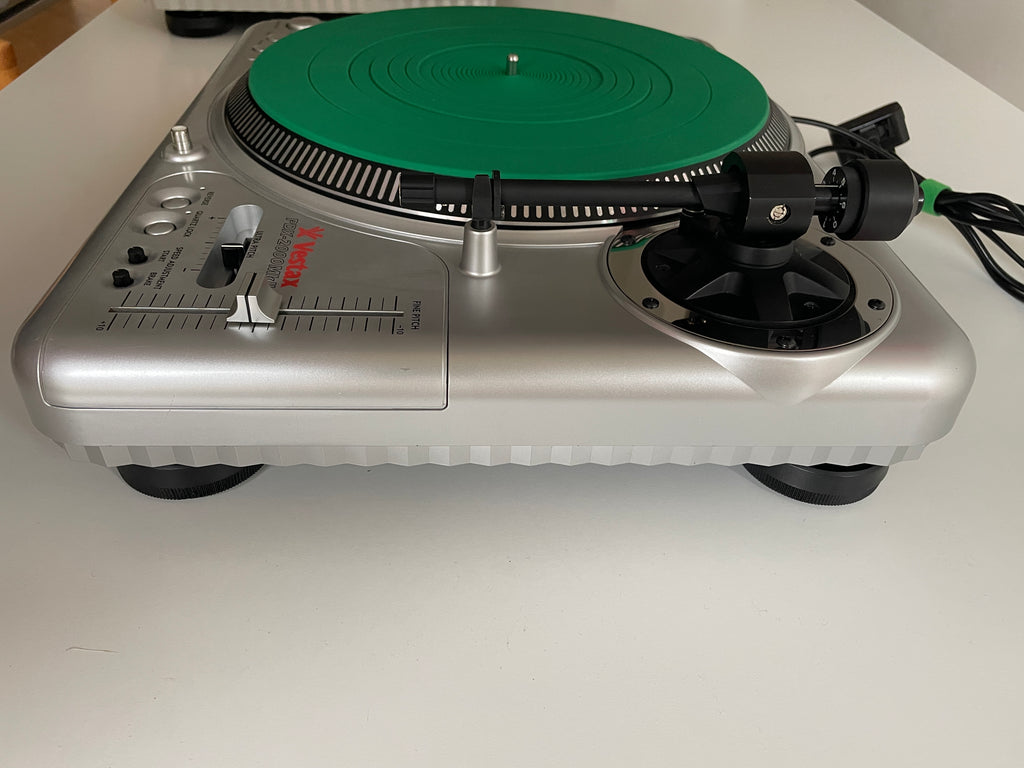 A silver portable turntable with a green vinyl record platter, photographed from above against a plain light background.