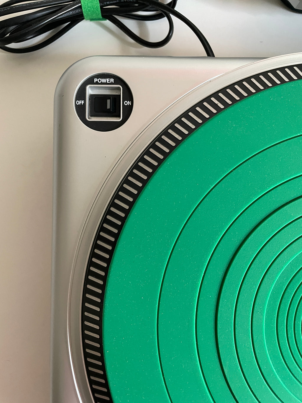 Close-up of a portable electric burner or hot plate with a silver base, a green circular heating element, a power switch, and a black power cord on a light surface.