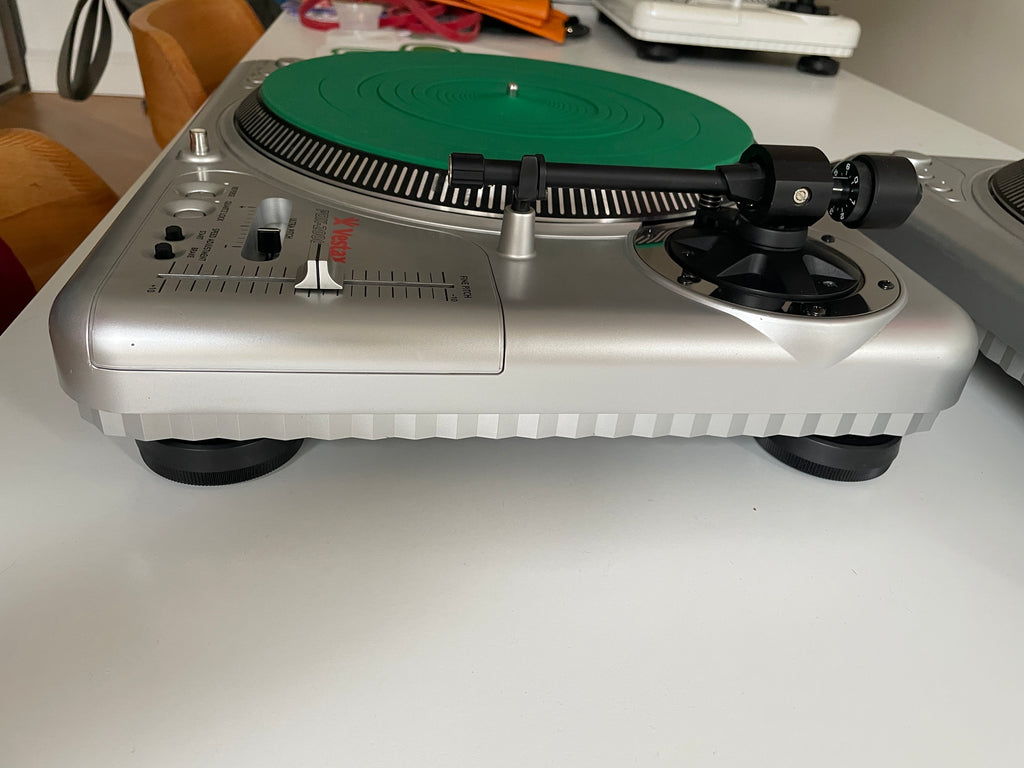 A silver turntable with a green vinyl record and black components, photographed from an angled overhead view against a white wall.
