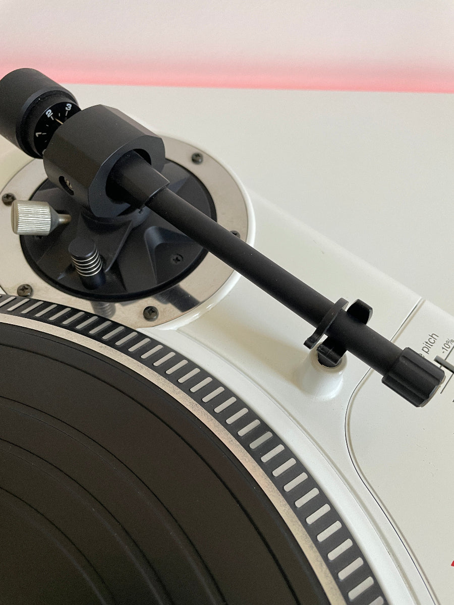Close-up of a turntable with a black arm and white platter.