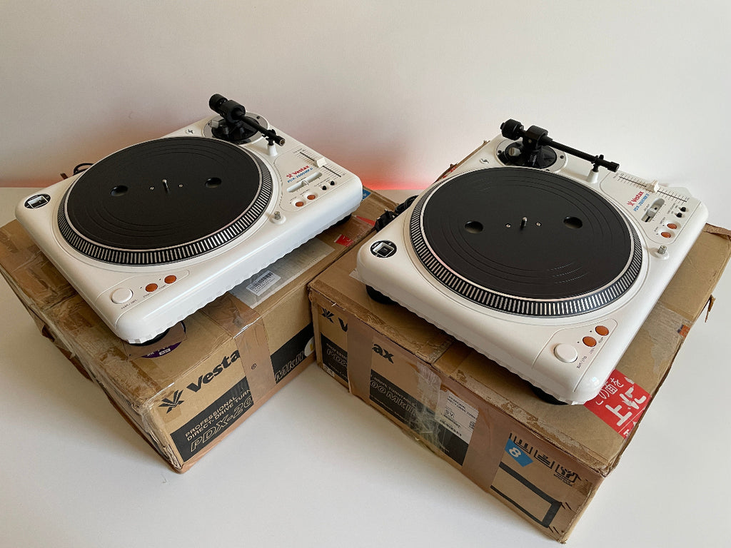 Two white turntables on cardboard boxes with a plain background
