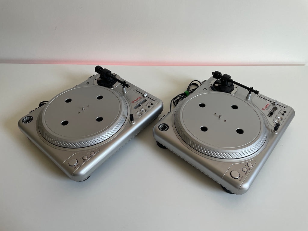 Two silver DJ turntables on a white surface with a red light in the background.